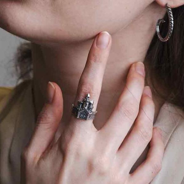 Photograph of the castle ring on an index finger. The index finger is leaning against the side of a chin.