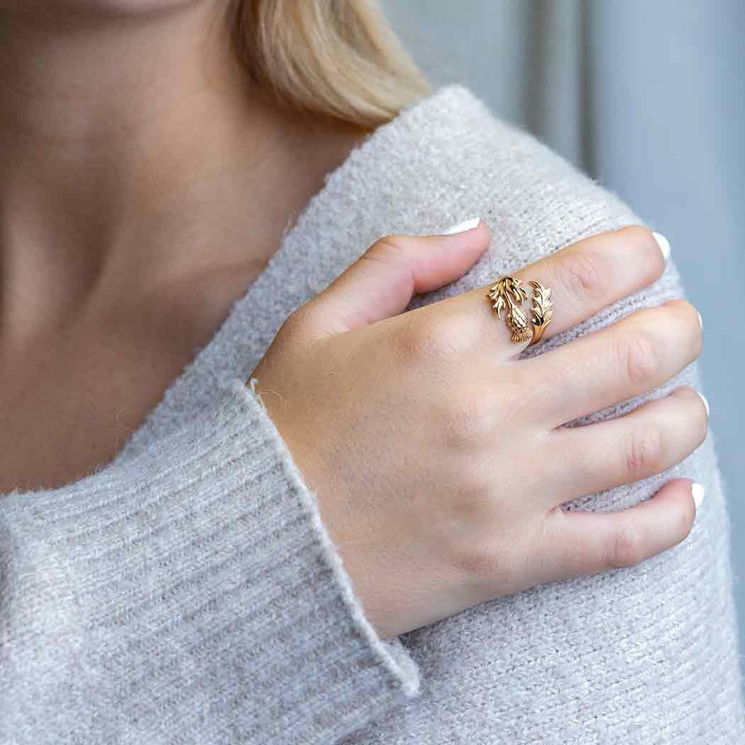 Bronze ring with thistle flower on an index finger of a right hand leaning on the left shoulder.