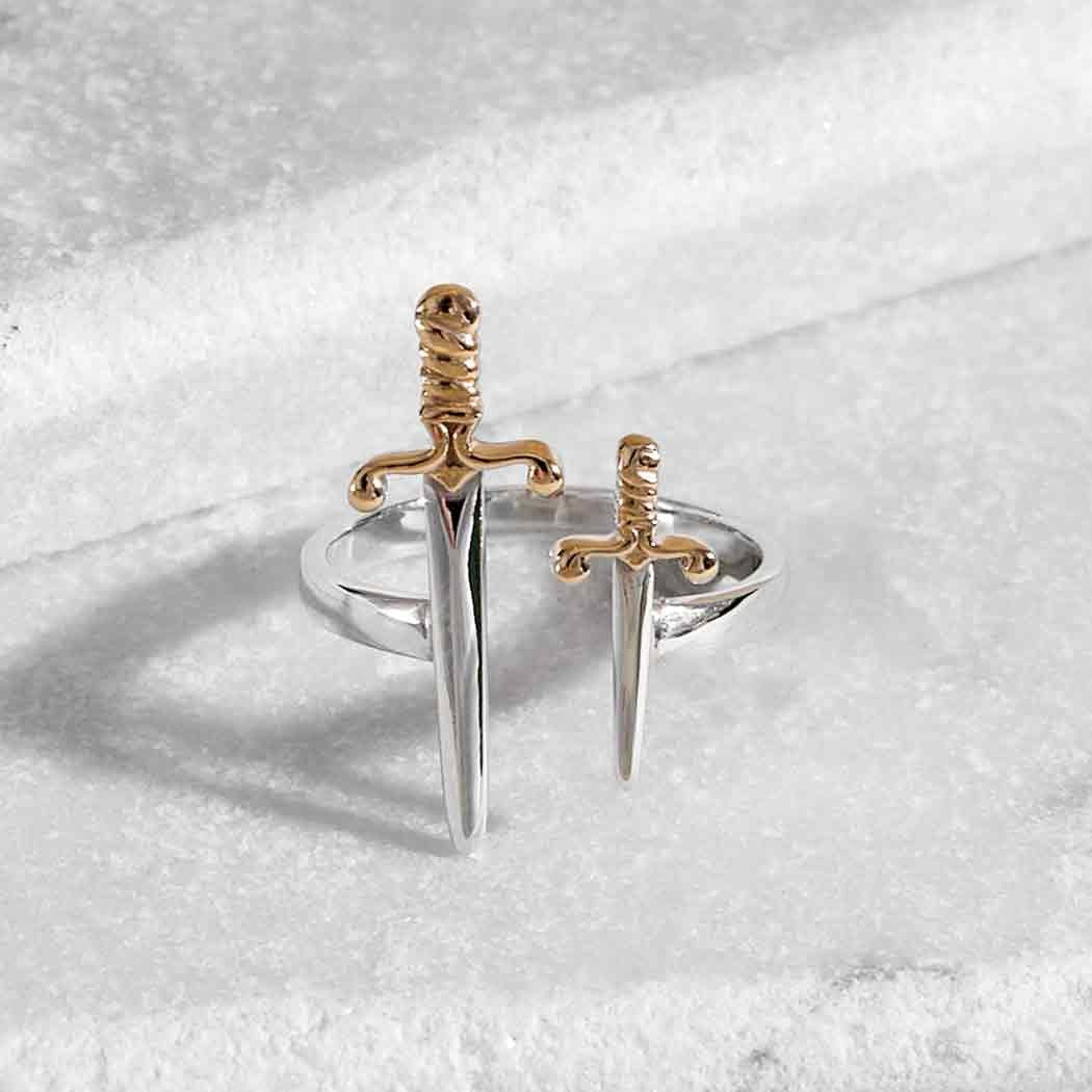 Photograph of a silver ring on a marble base. The ring has a large sword on the left and a small sword on the right. Between them is an opening so that the ring is adjustable. The swords have bronze hilts.
